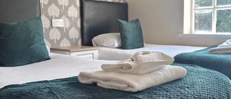 Una habitación de hotel con una cama, almohadas, cabecera, ventana y pared con diseño de hojas.