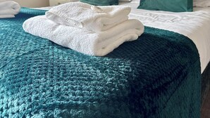 A neatly made bed with a teal blanket and white towels, green pillows, and a patterned wall in the background. - The Minworth Club & Lodge  (Sutton Coldfield)