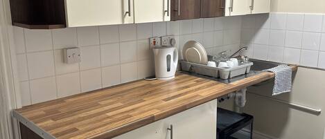Una cocina con armarios blancos, encimera de madera, una tetera y un caja de almacenamiento negra.