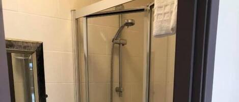 Une douche fermée par des parois en verre, dotée d’un pommeau de douche à main et d’un robinet mural.