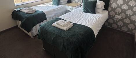 A hotel room with two beds, a window, and a patterned wallpaper.