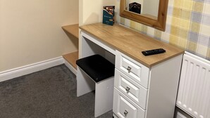 A small, compact bedroom with a wooden vanity, a mirror, a black stool, and a radiator. - The Minworth Club & Lodge  (Sutton Coldfield)