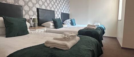 Habitación de hotel con dos camas, un papel tapiz estampado, una lámpara de techo y una ventana.