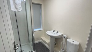 A bathroom with a glass shower enclosure, a white toilet, a pedestal sink, and a window. - The Minworth Club & Lodge  (Sutton Coldfield)
