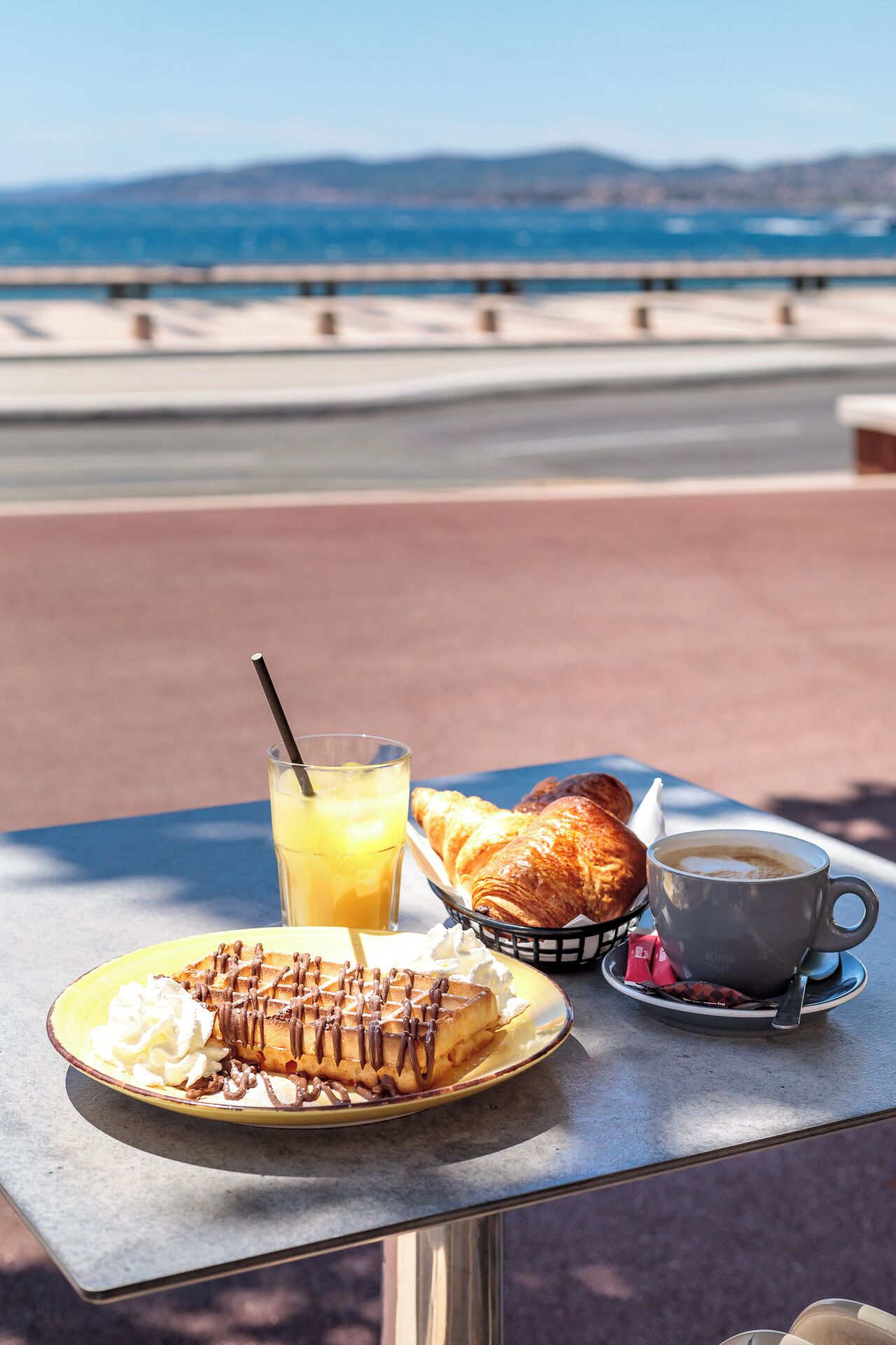 Una mesa con alimentos para el desayuno, como waffles, croissants, un vaso de jugo de naranja y una taza de café.