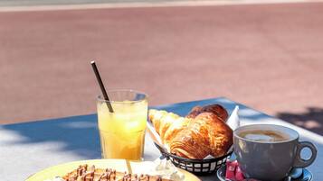 Una mesa con alimentos para el desayuno, como waffles, croissants, un vaso de jugo de naranja y una taza de café.