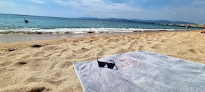 Uma praia com pegadas na areia, uma toalha e óculos de sol.