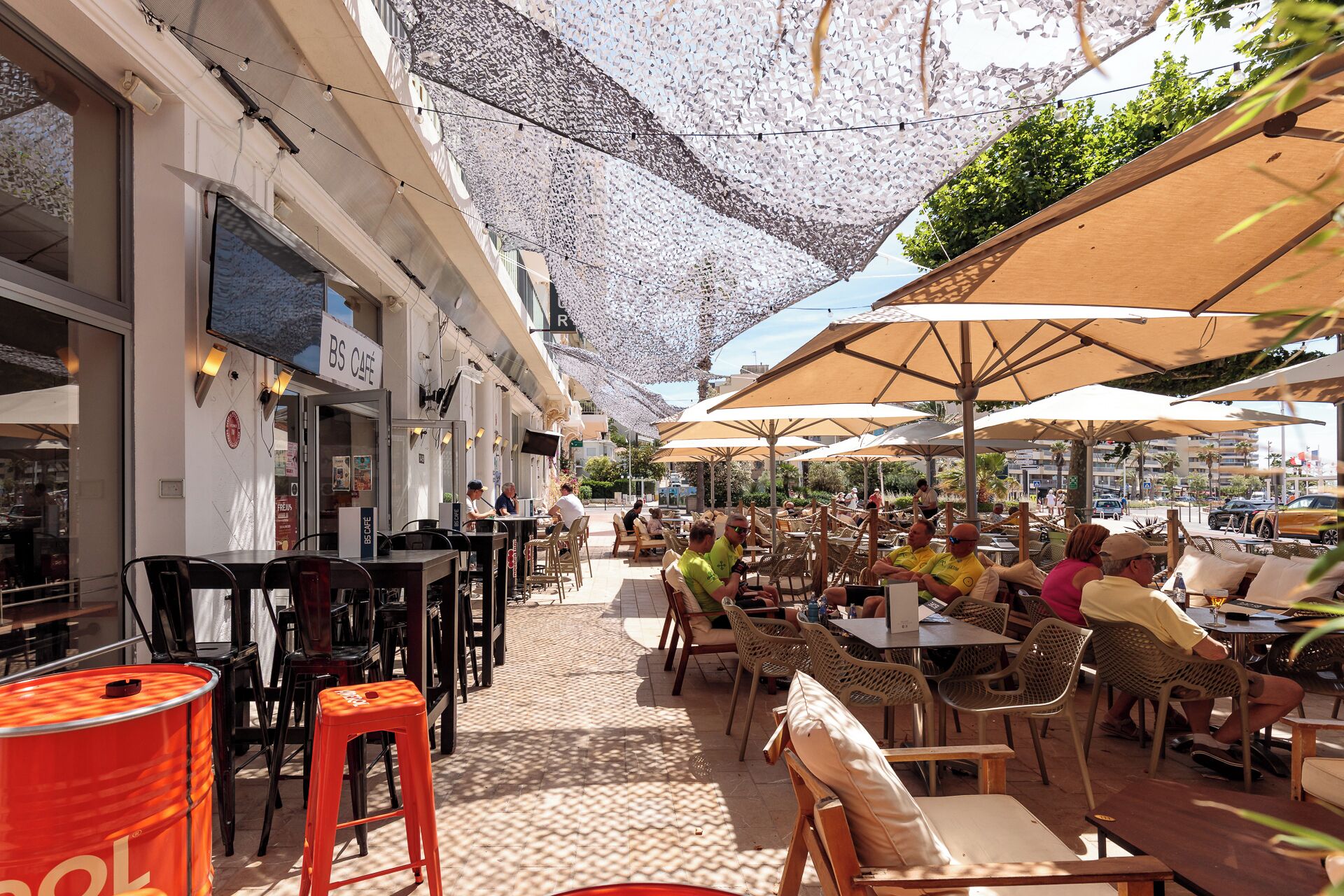 Egy szabadtéri kávézó, asztalokkal és székekkel, egy „BS CAFE” felirattal ellátott táblával és csempézett padlóval.