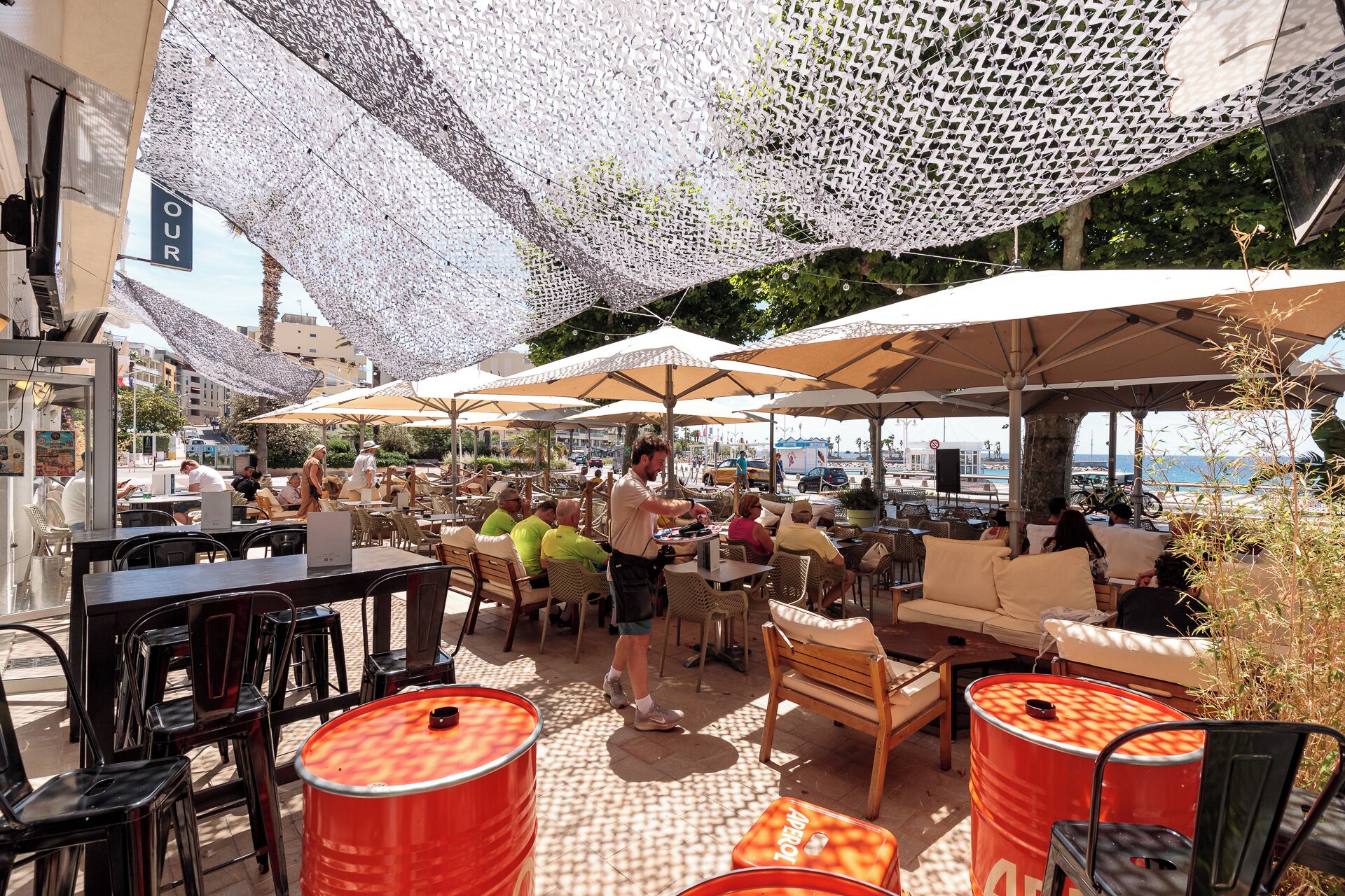 Un café en plein air avec des tables et des chaises, des parasols et des tonneaux rouges.
