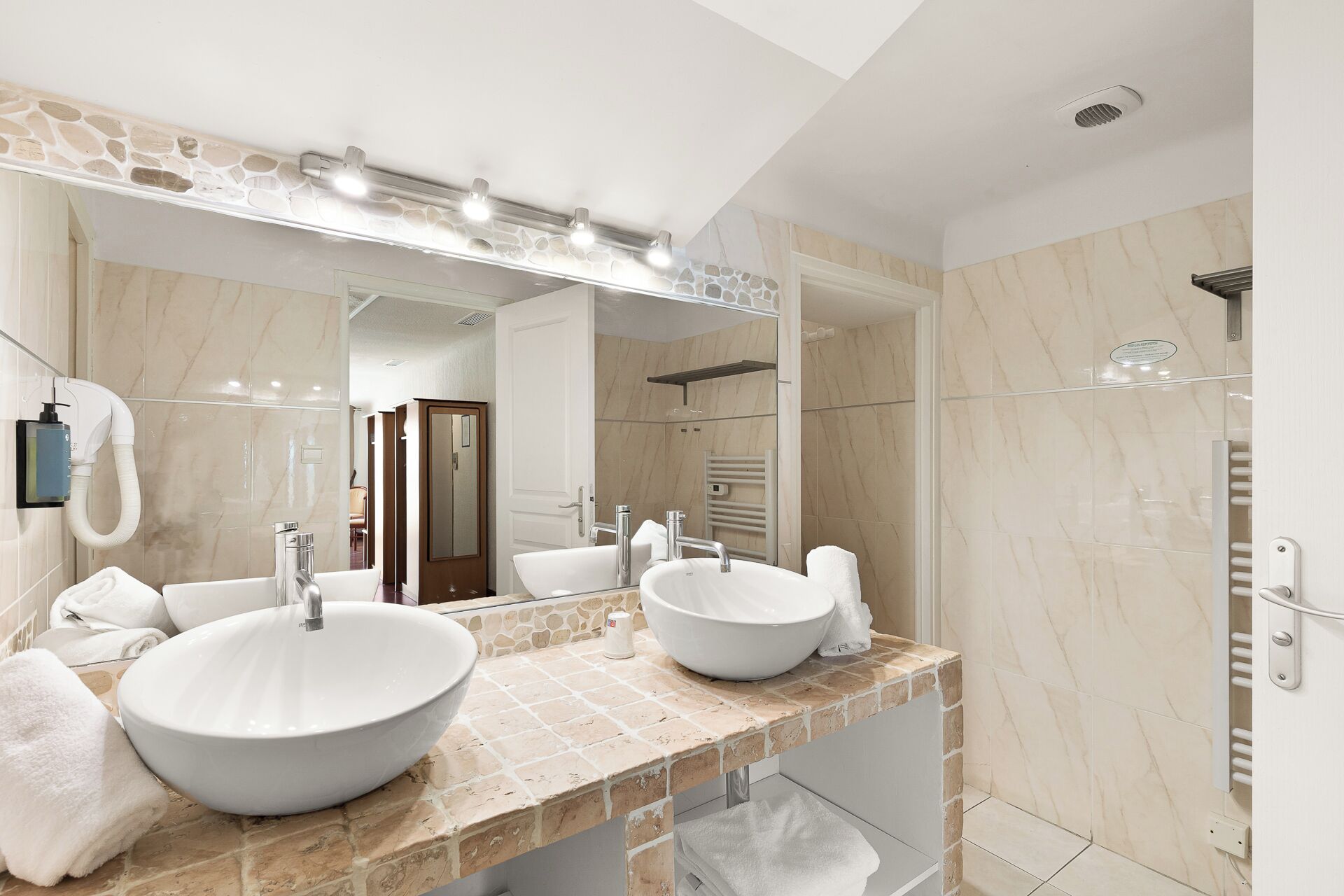 Une salle de bain moderne avec deux grands lavabos, un miroir avec éclairage intégré, un porte-serviettes et un espace douche.