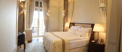 A hotel room with a large bed, bedside lamps, a desk with a chair, and a view of the outdoors through a window.