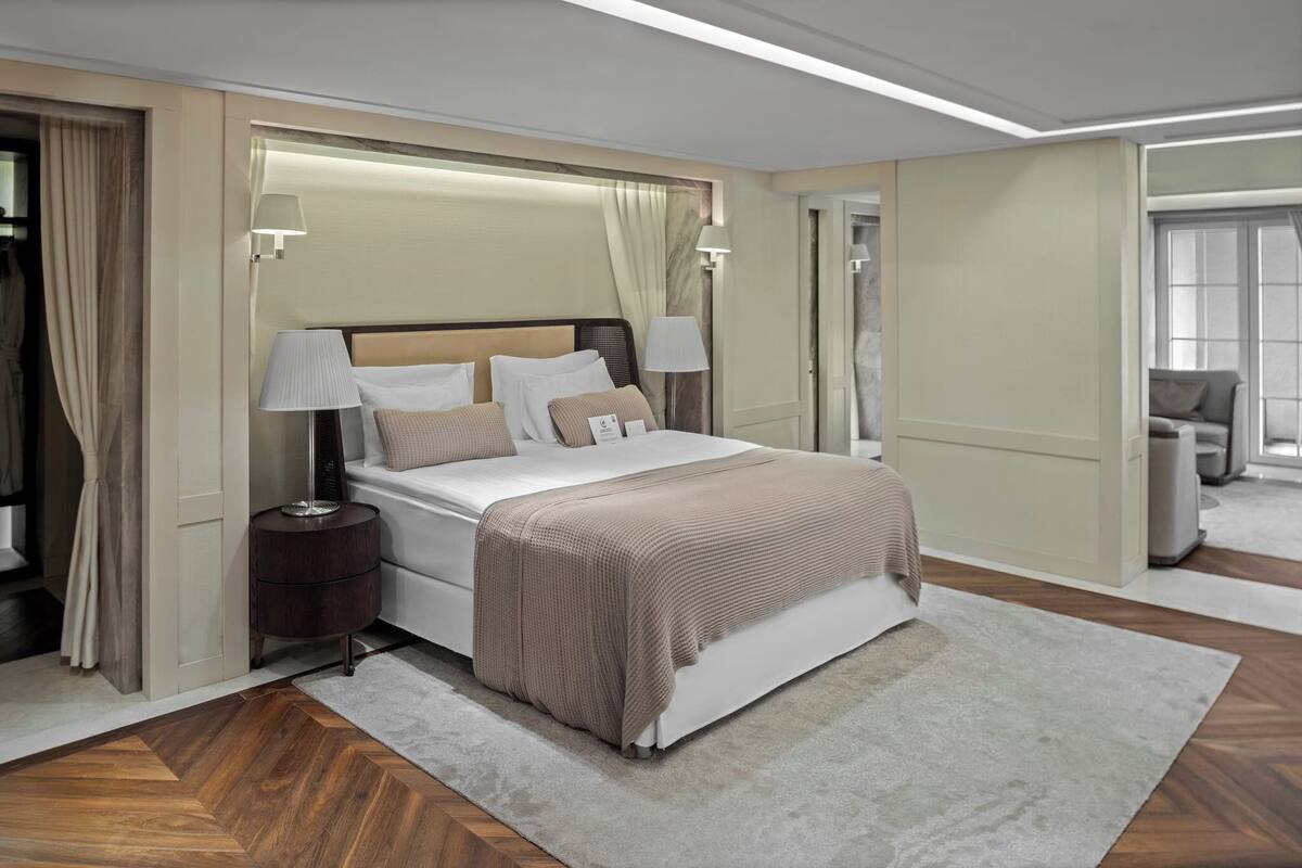 A modern hotel room with a large bed, bedside lamps, a nightstand, and a view of the hallway.