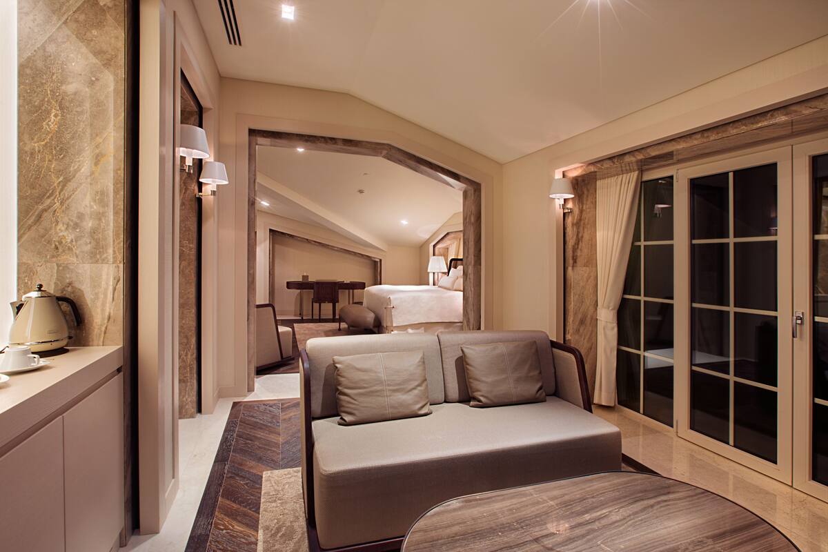 A modern hotel room with a large bed, a sitting area, and a separate dining space.