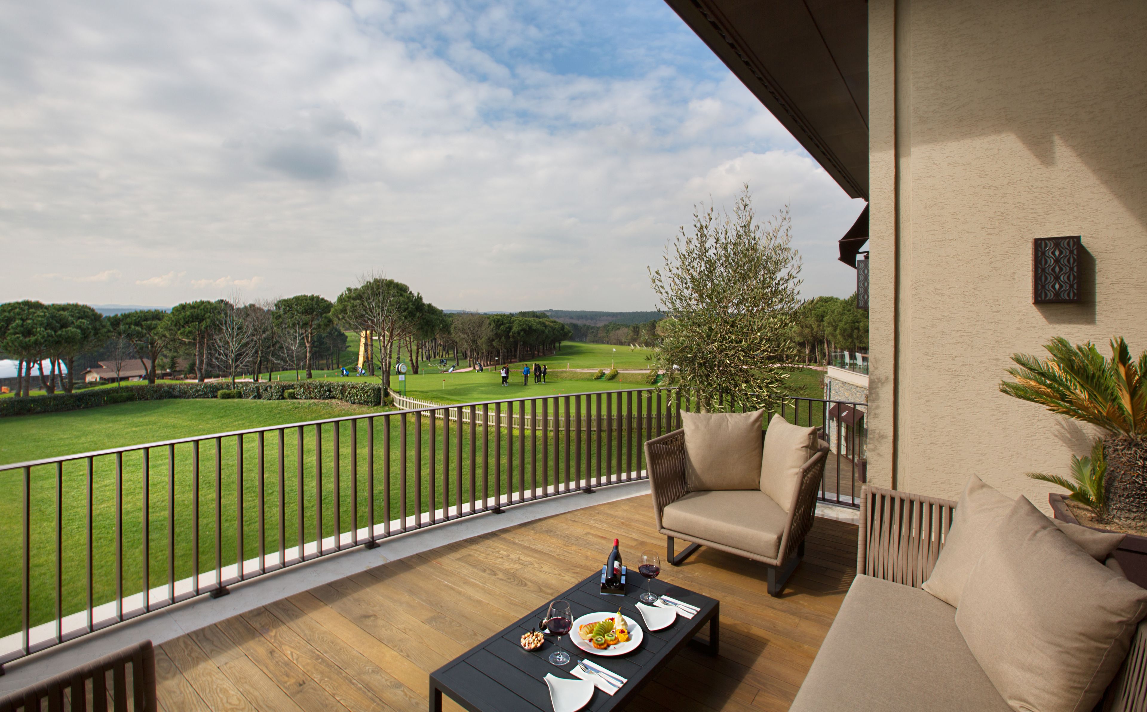 Ein Balkon mit Holzboden, einem Esstisch mit Tellern und Gläsern sowie Blick auf einen Golfplatz.