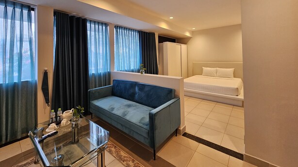 A hotel room with a bed, a sofa, a glass table with a vase, and a window with curtains.