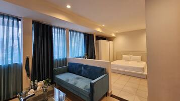 A hotel room with a bed, a sofa, a glass table with a vase, and a window with curtains.