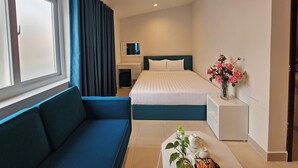 A hotel room with a bed, a sofa, a small table with a vase of flowers, and a desk with a chair.