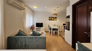 A modern living room with a sofa, a dining table with chairs, a TV, and a kitchen area with a microwave.