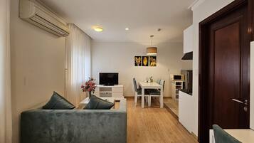 A modern living room with a sofa, a dining table with chairs, a TV, and a kitchen area with a microwave.
