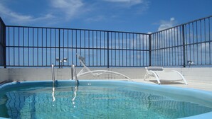 Une piscine dont le bord est recouvert de carrelage, une clôture en métal et, en arrière-plan, un ciel bleu dégagé.