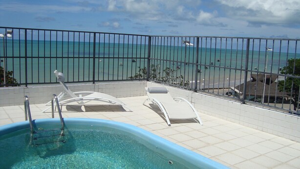 Une piscine sur le toit, avec une eau d’un bleu cristallin, des chaises longues blanches et une vue sur l’océan.