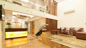A modern lobby with a reception desk, a staircase, a seating area with a sofa and coffee table, and a decorative plant. - Song Hung Hotel & Serviced Apartments (Ho Chi Minh City)