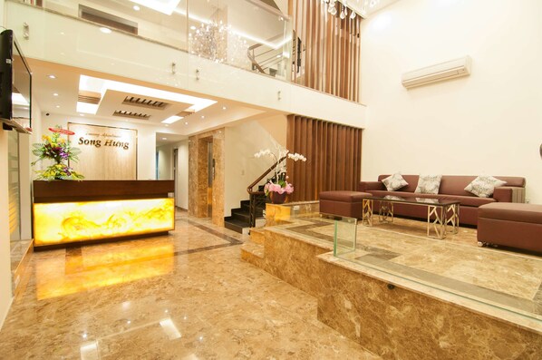 A modern lobby with a reception desk, a staircase, a seating area with a sofa and coffee table, and a decorative plant. - Song Hung Hotel & Serviced Apartments (Ho Chi Minh City)