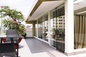 A balcony with a table and chairs, potted plants, and a view of a building through large glass doors. - Song Hung Hotel & Serviced Apartments (Ho Chi Minh City)