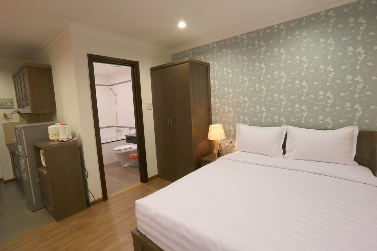 Ett hotellrum med en säng, en garderob, ett skrivbord med en lampa och ett badrum som syns genom en öppen dörr.