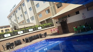 A hotel with a swimming pool, outdoor seating, and a sign indicating a massage service. - Jades Hotel (Abuja)