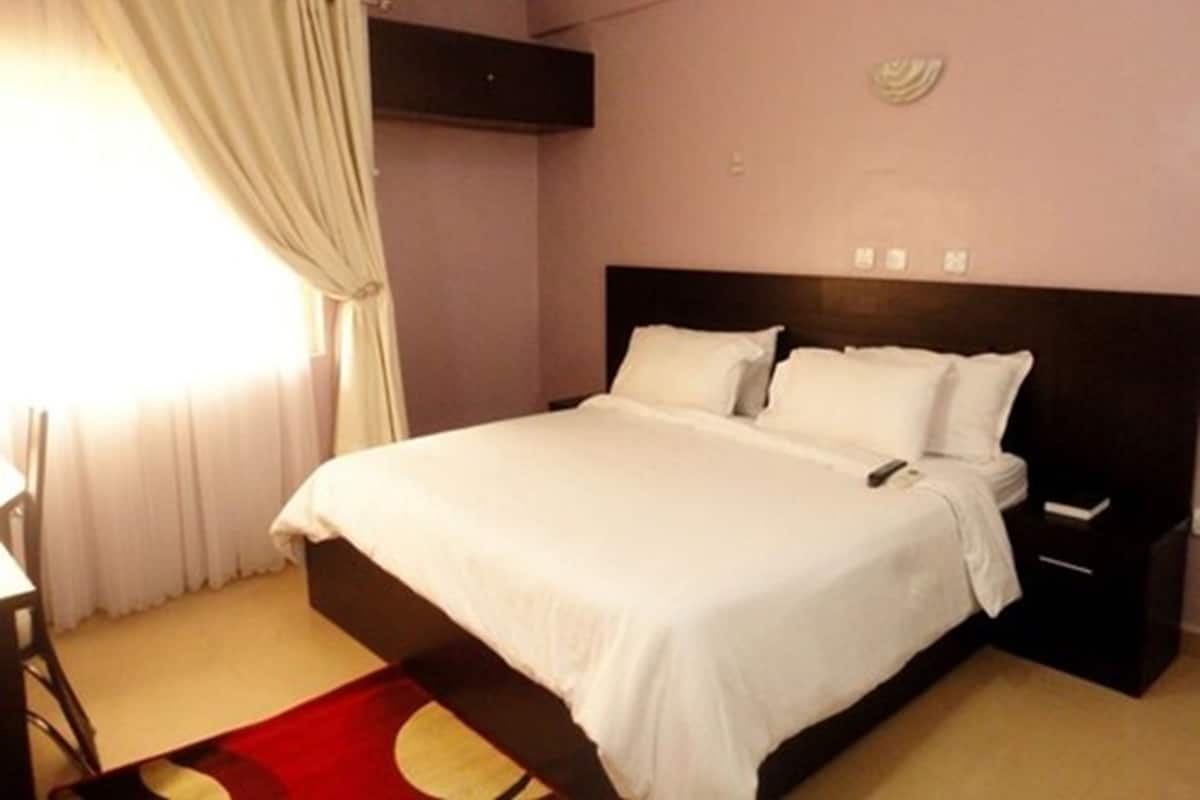 Habitación de hotel con una cama grande, una mesita de noche, una silla y una ventana con cortinas.