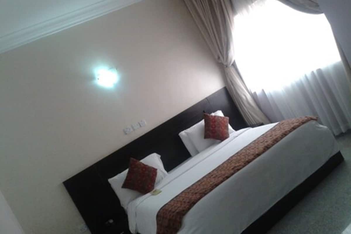Una habitación de hotel con cama, cortinas y una lámpara fijada a la pared.