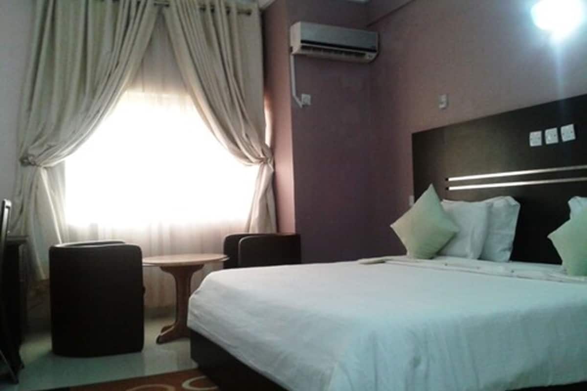 Una habitación de hotel con una cama, una mesita, una silla y un equipo de aire acondicionado.
