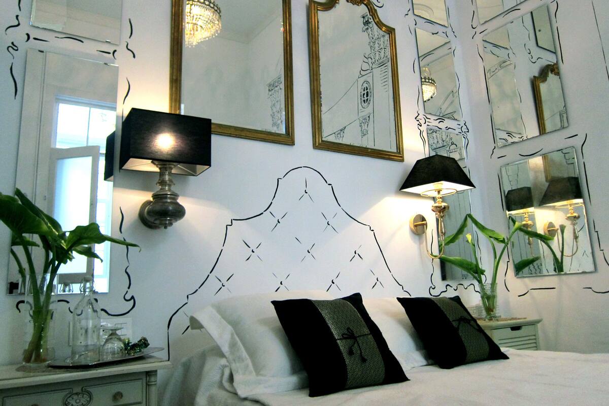 Une chambre à coucher avec un grand lit, deux lampes fixées au mur et plusieurs miroirs.