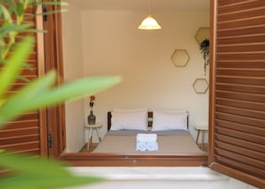 Un dormitorio con una cama, mesitas de noche, un florero con una flor y una lámpara colgante.
