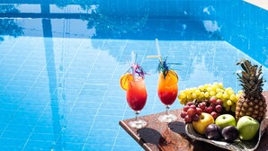 Escena junto a la piscina con dos bebidas, una bandeja de frutas y una piña.