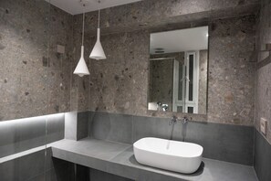 Un baño moderno con una bañera independiente, un espejo grande y lámparas colgantes.