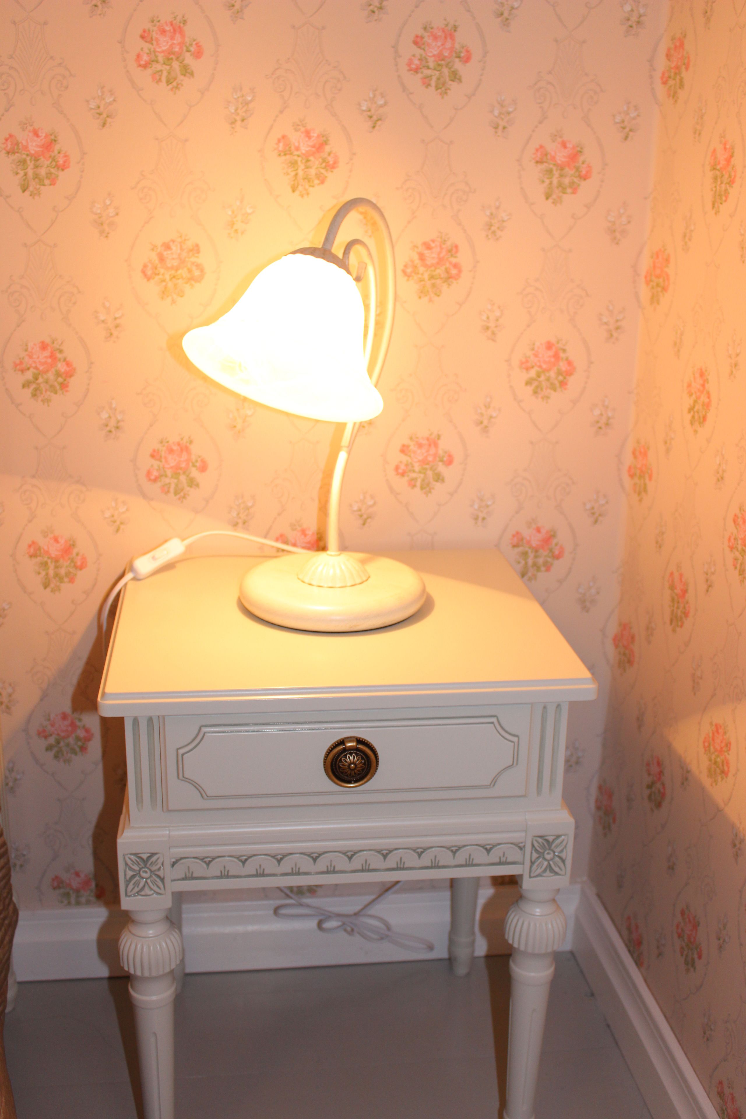 A white bedside table with a lamp, a drawer, and a decorative knob.