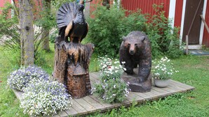 A wooden platform with a bear sculpture and a bird sculpture, surrounded by flowers and greenery.