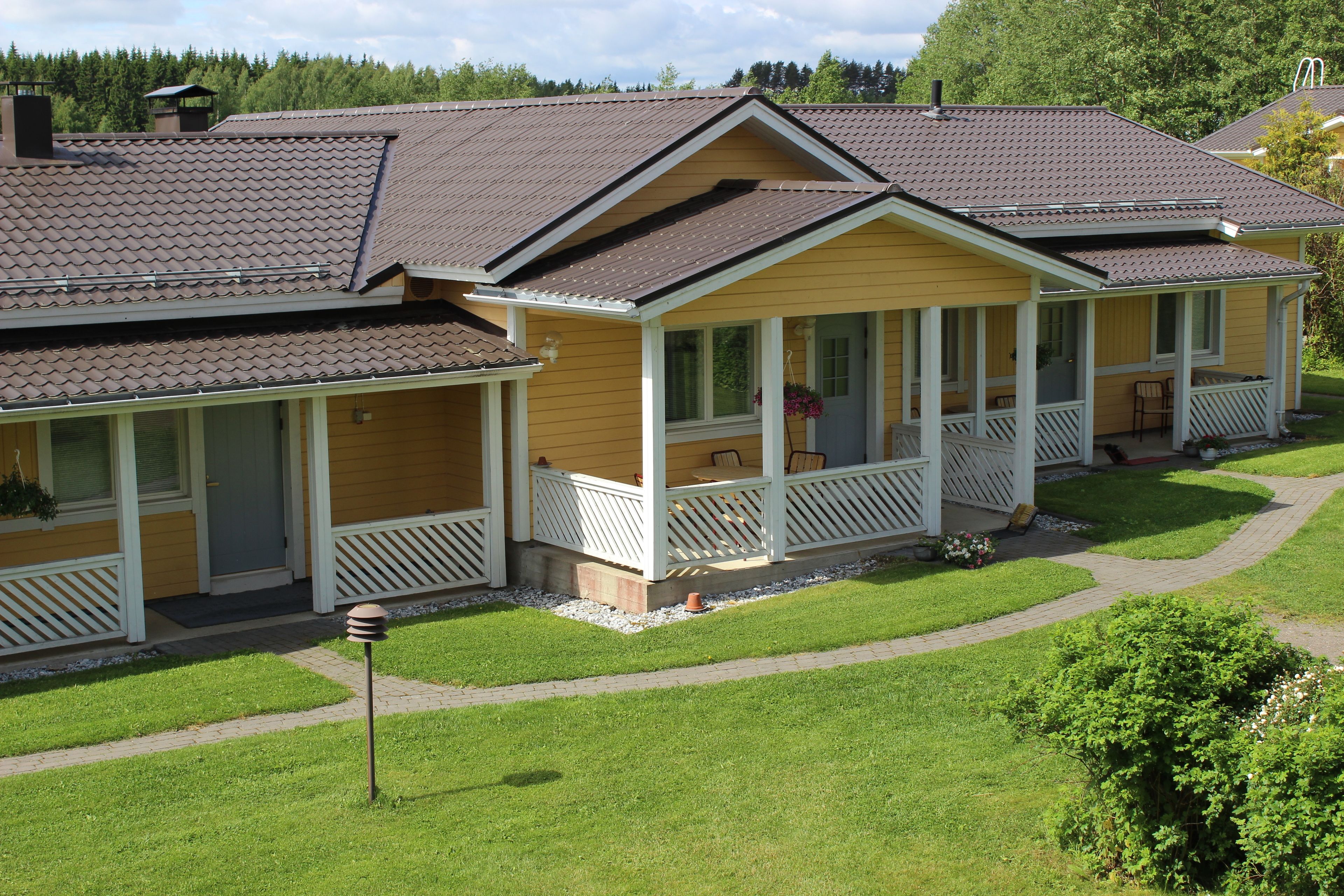 A row of yellow cabins with white railings, each with a porch and a small garden area.