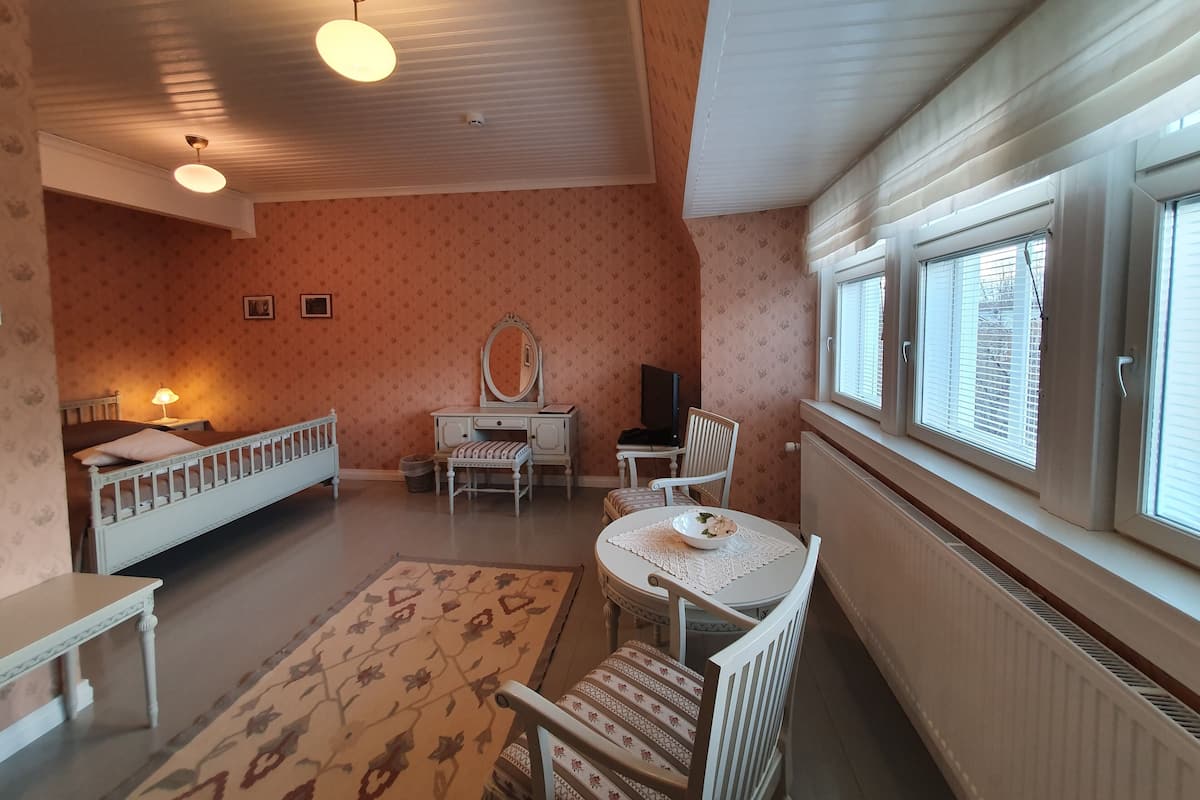 Ein gemütliches Schlafzimmer mit Bett, Schminktisch mit Spiegel, kleinem Tisch mit Schale und Fenster mit Jalousien.