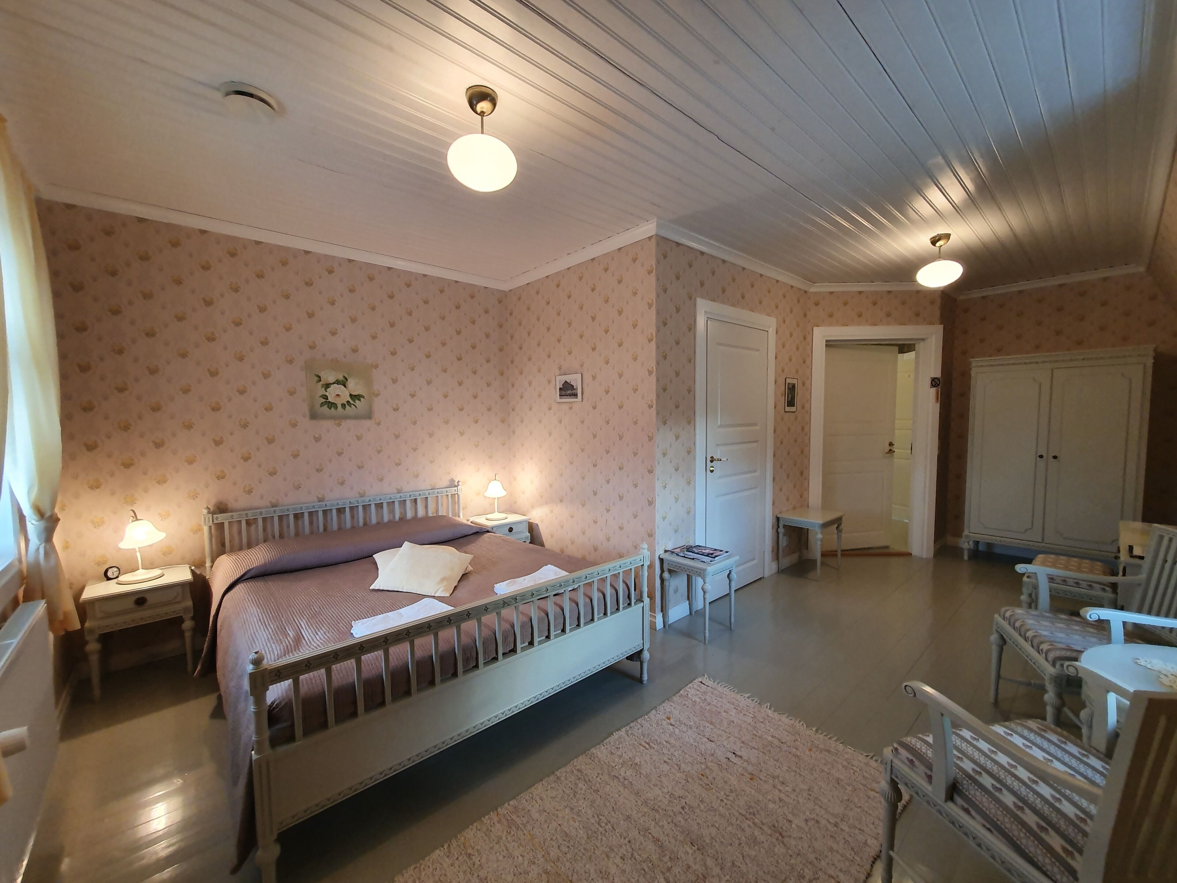Een slaapkamer met een bed, nachtkastjes, een stoel, een garderobe en een deur.