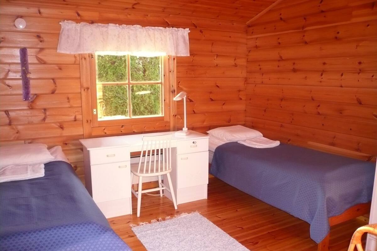 Eine Hütte mit zwei Betten, einem Schreibtisch, einem Stuhl und einem Fenster.