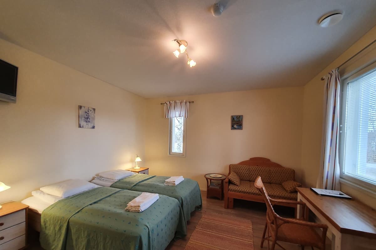 Ein Schlafzimmer mit zwei Betten, einem Schreibtisch, einem Stuhl, einem kleinen Tisch und einem Fenster mit Vorhängen.