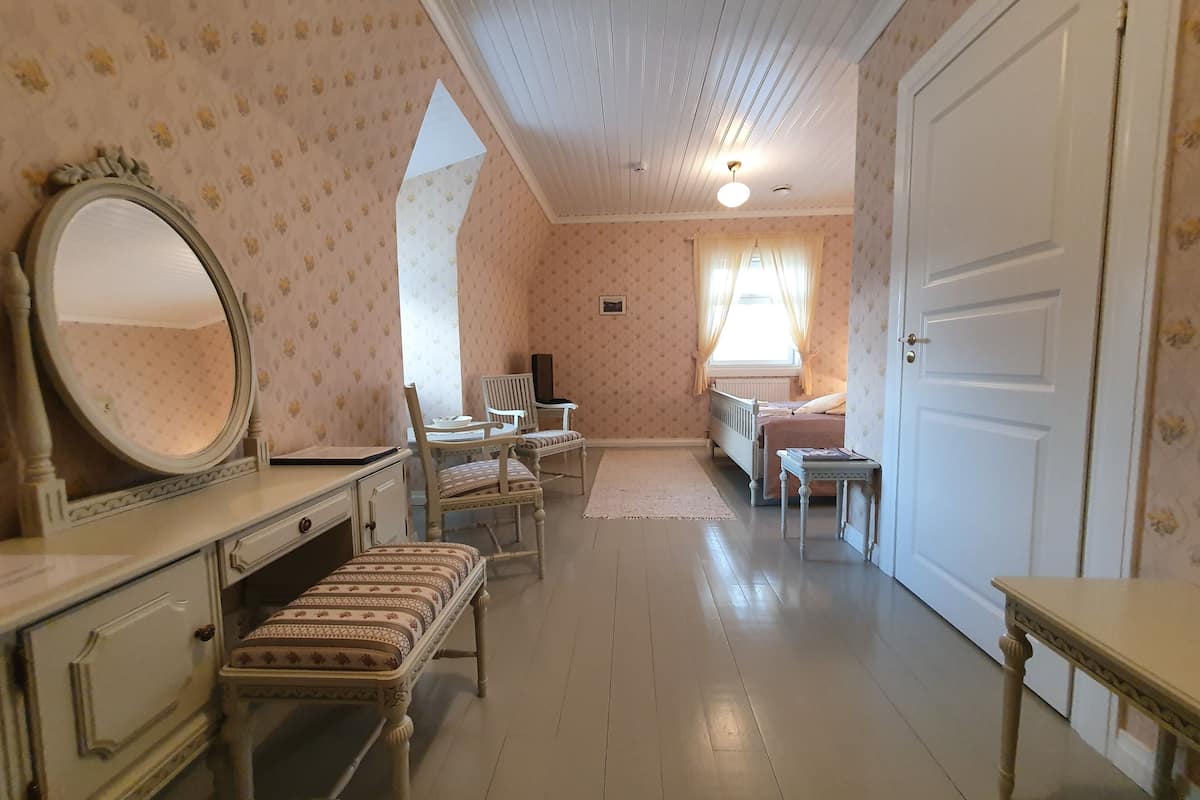 Ein Schlafzimmer mit einem Bett, einem Sessel, einem Schreibtisch mit Spiegel und einer Kommode.