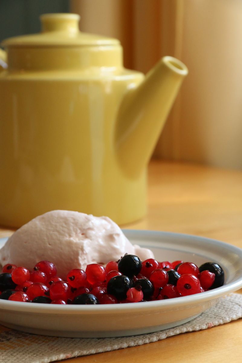 Une assiette avec de la glace et des fruits rouges, une théière jaune et une table en bois.
