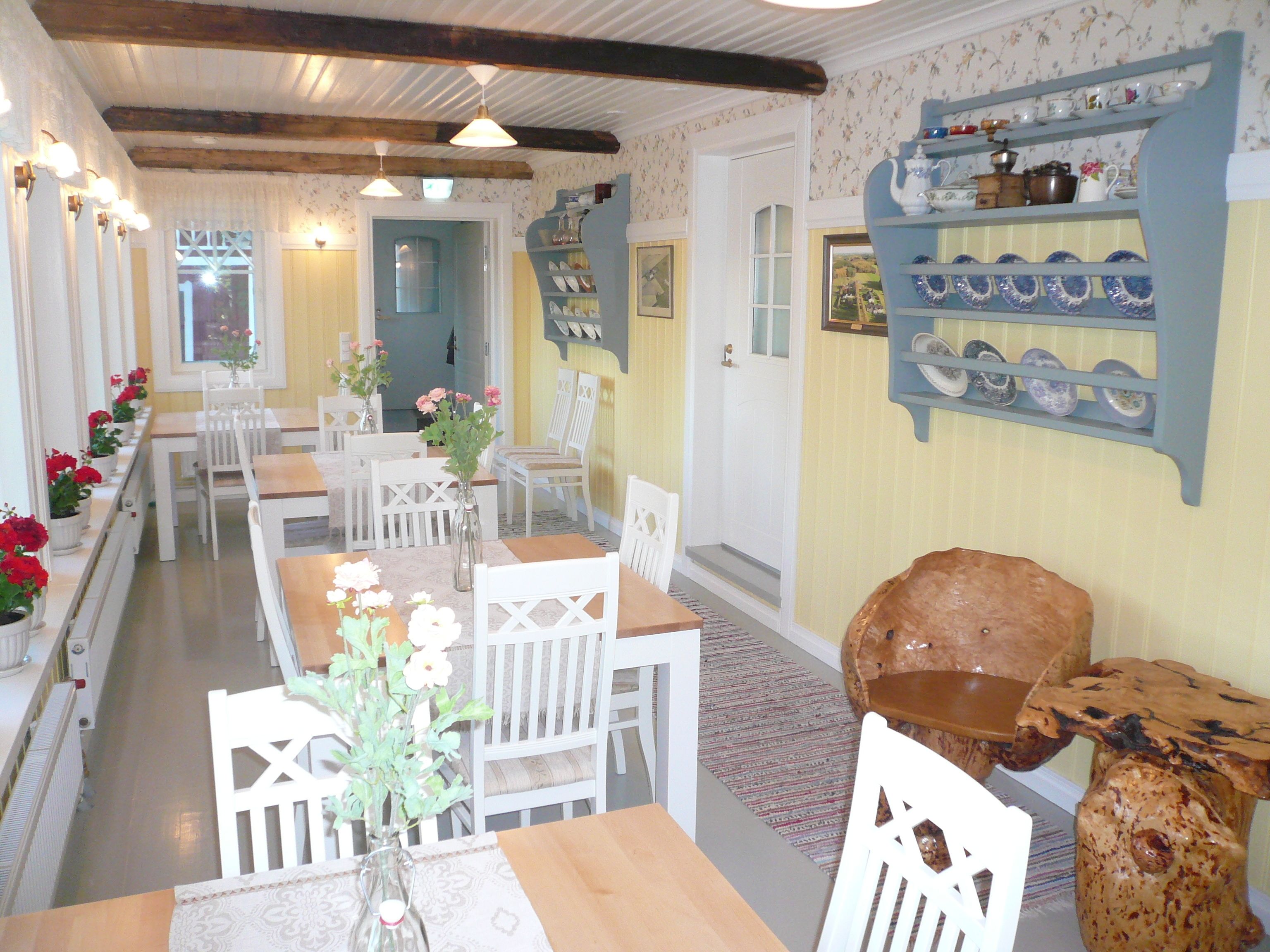 A dining area with white furniture, a vase with flowers, and a shelf with dishes.