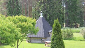 A log cabin with a conical roof surrounded by a well-maintained garden and tall trees.