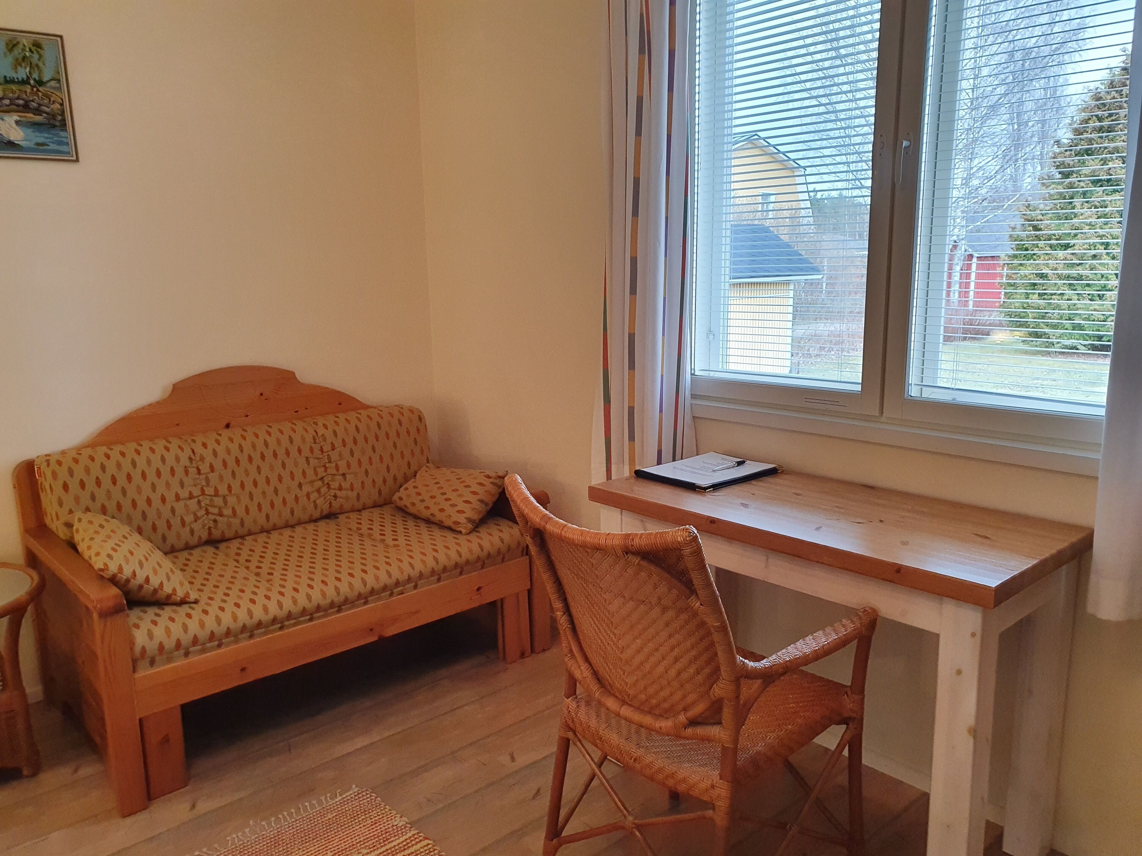A cozy room with a wooden sofa, a wicker chair, and a wooden desk with a window.