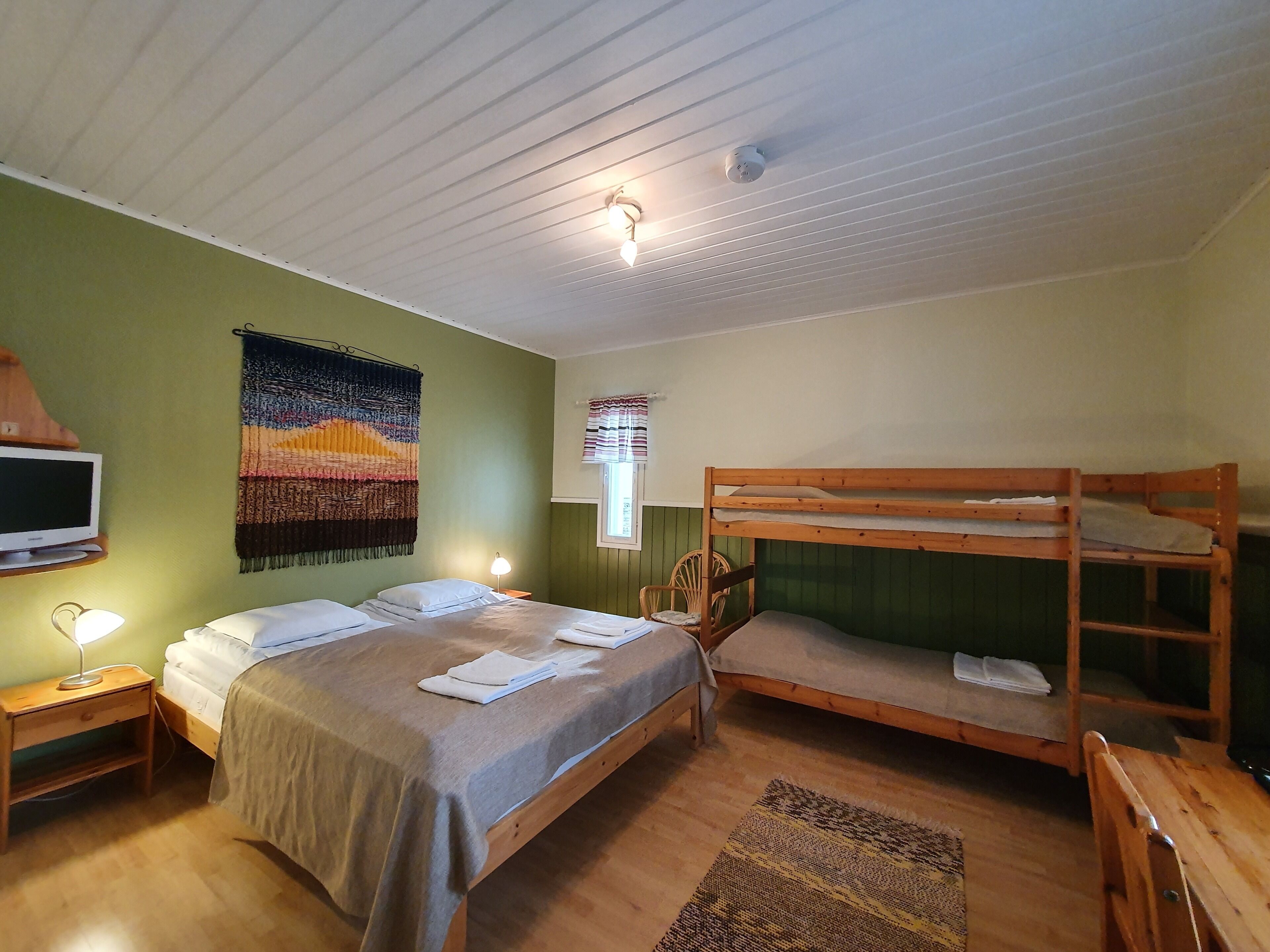 Ein Zimmer mit einem Etagenbett, einem Einzelbett, einem Fernseher, einer Lampe und einer Wandteppich.